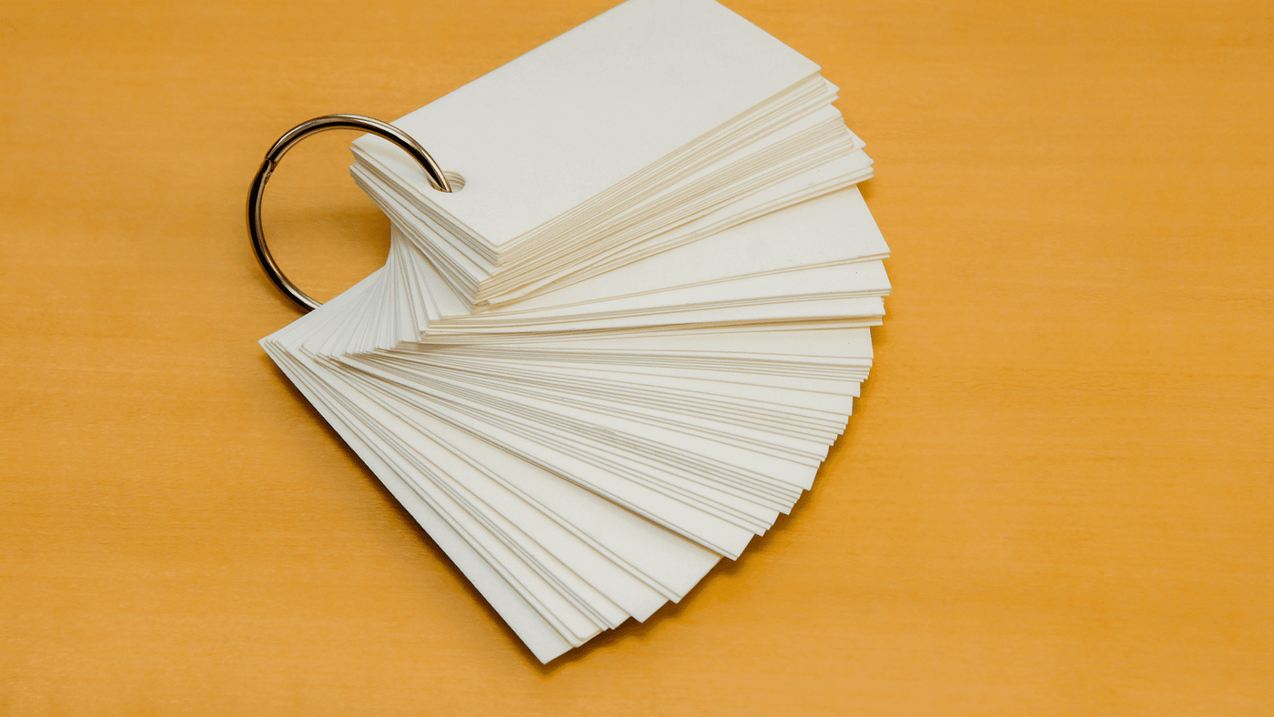 A stack of blank flashcards fanned out on a wooden surface, held together by a metal ring.