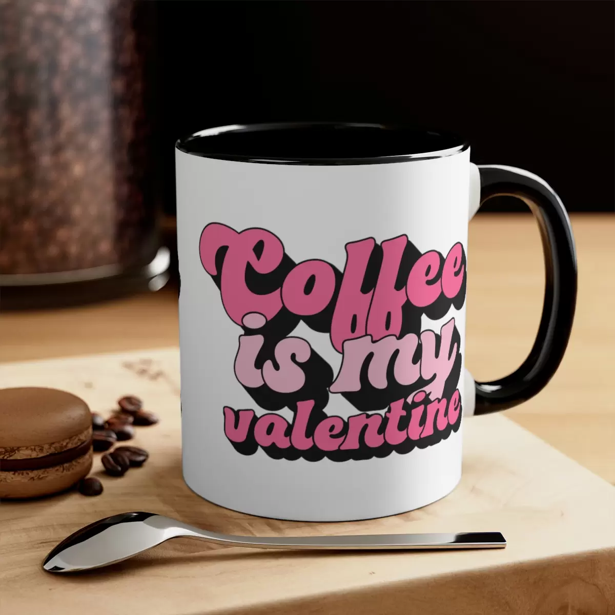 White coffee mug with black handle, featuring pink text that reads "Coffee is my valentine," placed on a wooden surface with