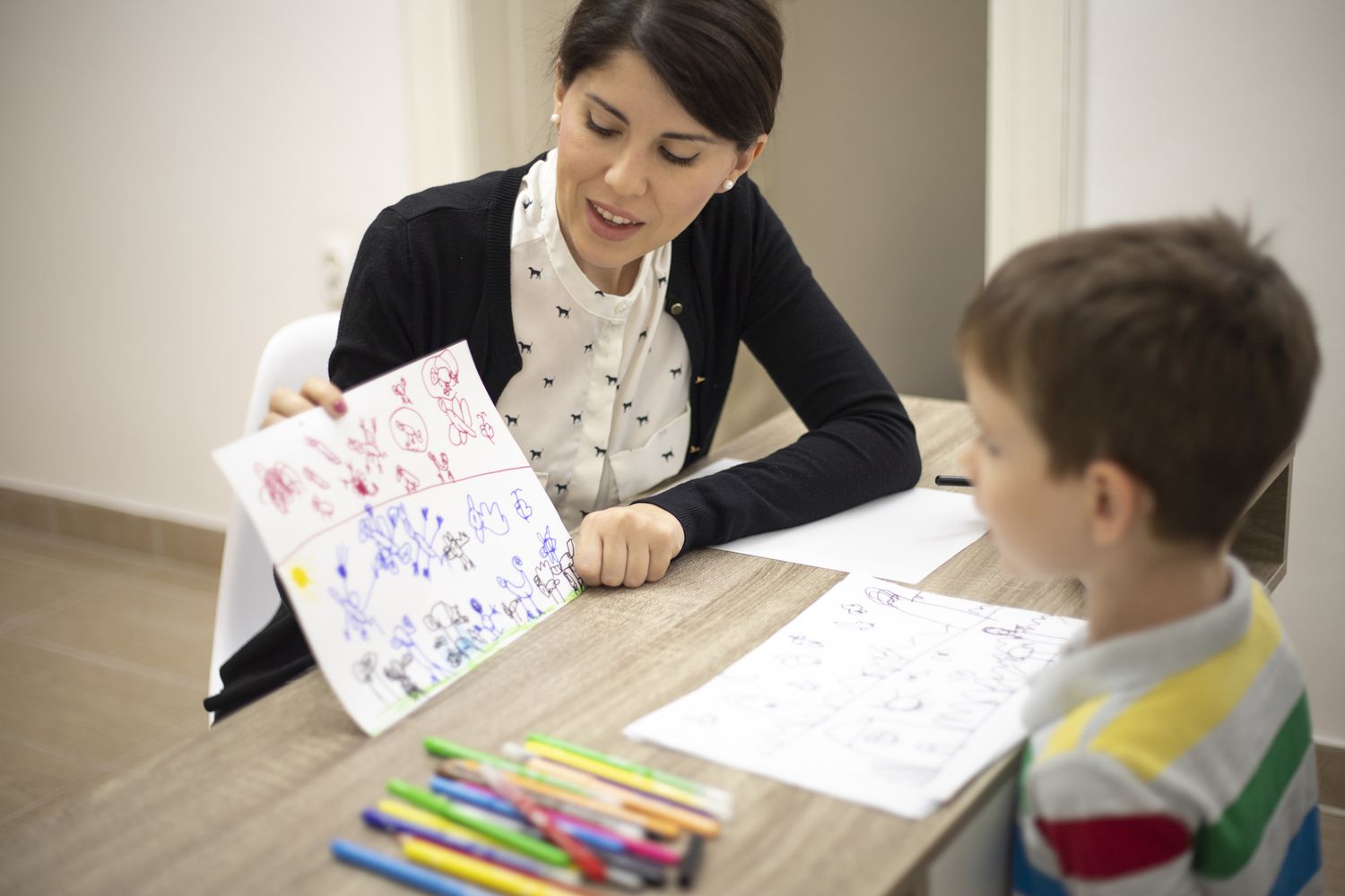 A therapist shows a child colorful drawings during a session focused on addressing sleep problems.
