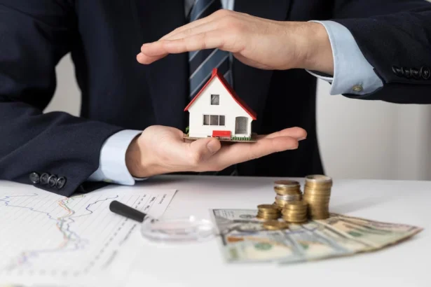 A businessman in a suit holds a small model house while surrounded by cash and coins, symbolizing investment financing.