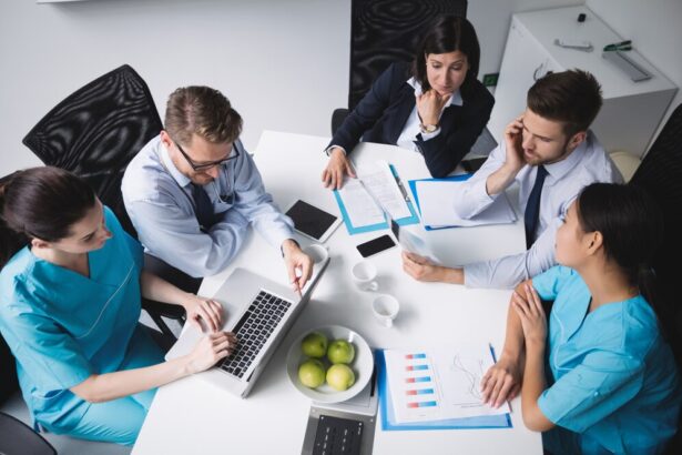 Healthcare professionals in a meeting, discussing documents and data on a table with laptops, charts, and apples.
